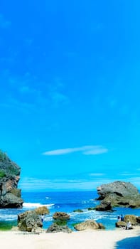 A serene beach setting with clear blue skies, rocks, and gentle sea waves. Perfect for representing relaxation, nature, and tranquility in a coastal environment.