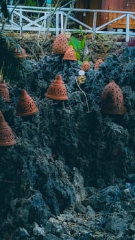 Decorative terracotta pots placed on rugged, rocky terrain juxtaposed with lush green foliage, creating a rustic and artistic outdoor scene. Ideal for themes of nature, craftsmanship, and aesthetics.