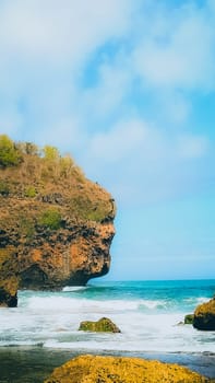 A serene beach setting with clear blue skies, rocks, and gentle sea waves. Perfect for representing relaxation, nature, and tranquility in a coastal environment.