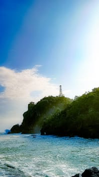 A rocky shoreline with a large rock formation in the background. The water is calm and the sky is blue