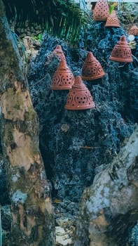 Decorative terracotta pots placed on rugged, rocky terrain juxtaposed with lush green foliage, creating a rustic and artistic outdoor scene. Ideal for themes of nature, craftsmanship, and aesthetics.