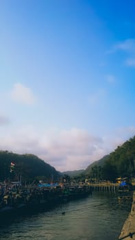 A large group of boats are floating on a lake. The sky is blue with some clouds