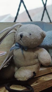 A teddy bear is sitting on a wooden surface next to a blue blanket. The scene is cozy and inviting, with the teddy bear looking up at the camera