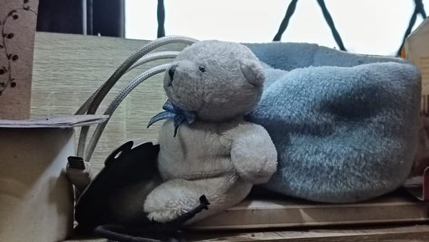 A teddy bear is sitting on a wooden surface next to a blue blanket. The scene is cozy and inviting, with the teddy bear looking up at the camera