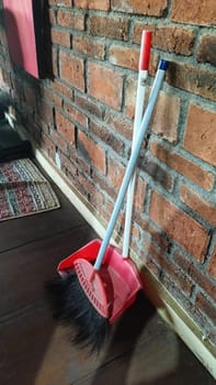 A red dustpan and broom resting against a rustic brick wall, creating a cozy and practical cleaning setup. Perfect for housekeeping and cleaning concepts.