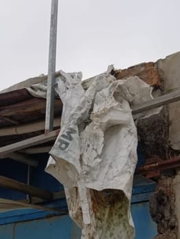 A tattered tarpaulin hangs on a rustic building, conveying deterioration and abandonment. Its worn texture tells a story of weather exposure and decay at a desolate construction site.