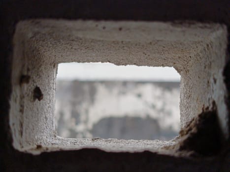 Abstract view through a grid of concrete blocks, showcasing the interplay of light and shadow. The geometric pattern offers an industrial and textured aesthetic, creating a sense of confinement and openness.