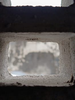 Abstract view through a grid of concrete blocks, showcasing the interplay of light and shadow. The geometric pattern offers an industrial and textured aesthetic, creating a sense of confinement and openness.