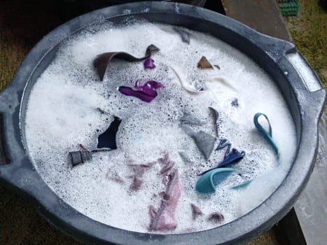 Various clothes soaking in soapy water inside three different colored buckets, depicting a traditional hand washing scene. Vibrant hues and textures convey a simple yet effective laundry method.