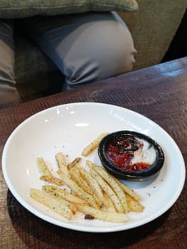 A bowl of savory French fries seasoned with herbs, accompanied by ketchup and mayonnaise, served on a rustic wooden table. Perfect for snack time or a casual dining setting.