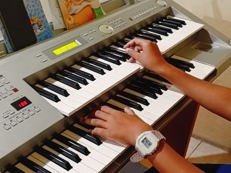 Close-up of young hands skillfully playing an electronic organ, capturing a moment of musical practice and creativity in a cozy music room.