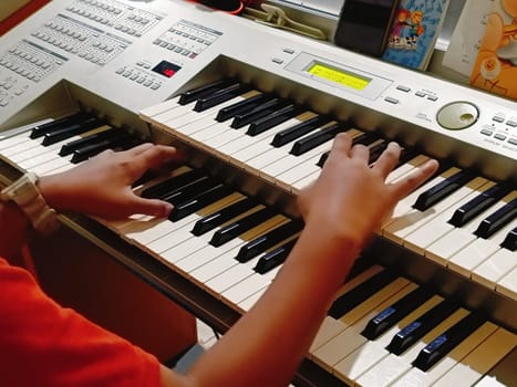 Close-up of young hands skillfully playing an electronic organ, capturing a moment of musical practice and creativity in a cozy music room.