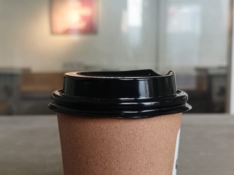Simple brown paper coffee cup with black plastic lid, ideal for takeaway beverages. Represents convenience, modern lifestyle, and daily routines. Perfect for cafes and coffee shops imagery.