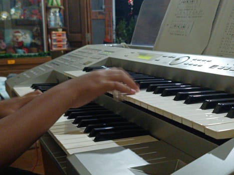 Close-up of young hands skillfully playing an electronic organ, capturing a moment of musical practice and creativity in a cozy music room.