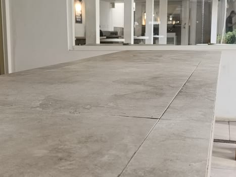 A modern minimalist cafe interior featuring a large concrete table and greenery. The bright space is filled with natural light, providing a serene and inviting atmosphere.