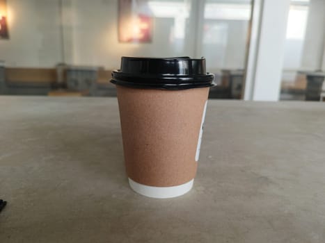 Simple brown paper coffee cup with black plastic lid, ideal for takeaway beverages. Represents convenience, modern lifestyle, and daily routines. Perfect for cafes and coffee shops imagery.