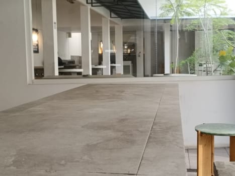 A modern minimalist cafe interior featuring a large concrete table and greenery. The bright space is filled with natural light, providing a serene and inviting atmosphere.