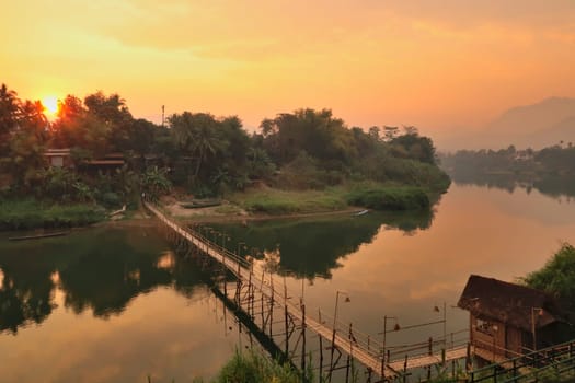 Spectacular view on a traditional bamboo bridge over the Nam Khan River at golden hour, sunset, Luang Prabang, Laos 2023