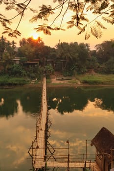 View onto a traditional bamboo bridge over the Nam Khan River at sunset, golden hour, Luang Prabang, Laos 2023