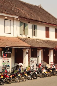 Many motorbikes are parked in front of a traditional, colonial house in the old town of Luang Prabang, Laos 2023