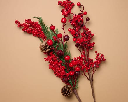 Decorative Christmas branch with red berries and pine cones on a brown background, top view