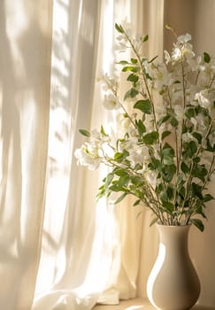 Morning sun shines through sheer curtains, highlighting a vase filled with delicate white flowers placed on a windowsill.