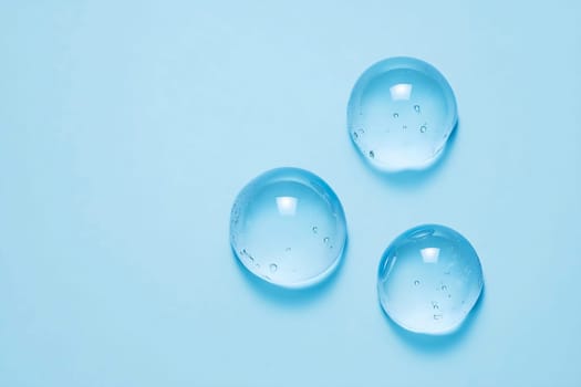 Three clear water droplets rest on a soft blue surface, showcasing their round shapes and reflections in a tranquil manner.
