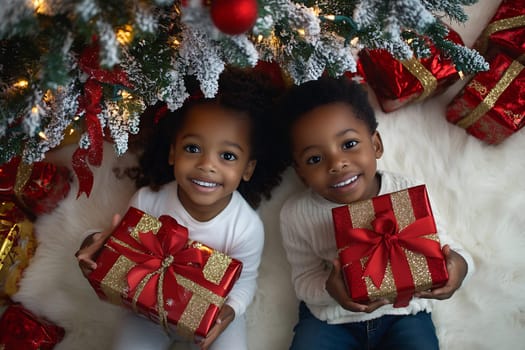 Two smiling kids cherish wrapped presents beneath a vibrant Christmas tree adorned with ornaments and sparkling lights.