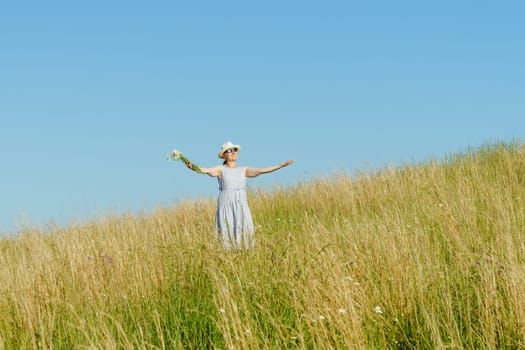Happy mature woman with wildflowers in a tall grass field on a bright summer day.