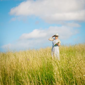 Happy mature woman with wildflowers in a tall grass field on a bright summer day.