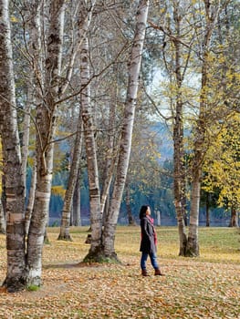 A woman in a stylish coat and a red scarf strolls through a beautiful park in autumn in eastern Washington.