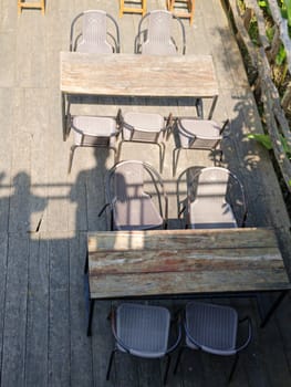 Top view of empty rustic wooden tables with chairs on an outdoor wooden deck, creating a serene and inviting atmosphere. There is also shadows of people from a rooftop