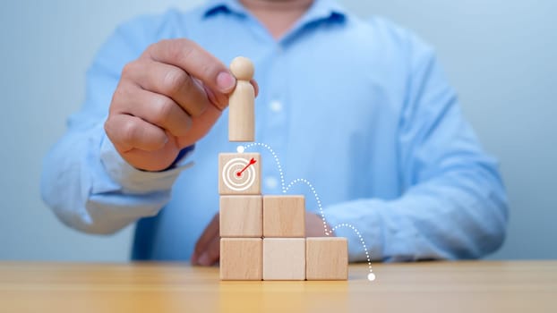 Hand man place wooden top of state or the winner, Concept of success, Winning and accomplishment in business. A man holding wooden doll model standing on target icon, Leadership and superiority.