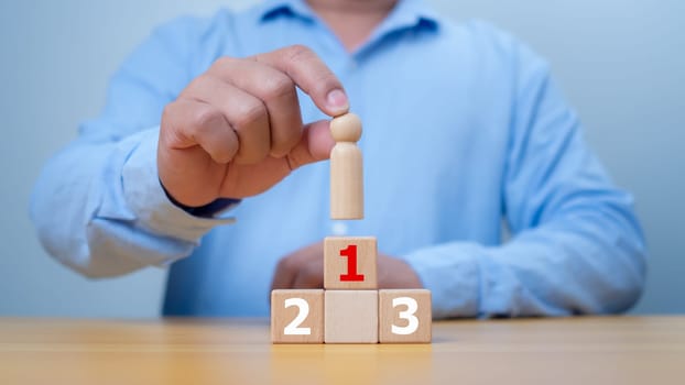 Hand man place wooden top of state or the winner. Concept of success, Winner and victory in business. A man holding wood person model standing on award podium, Leadership and superiority.