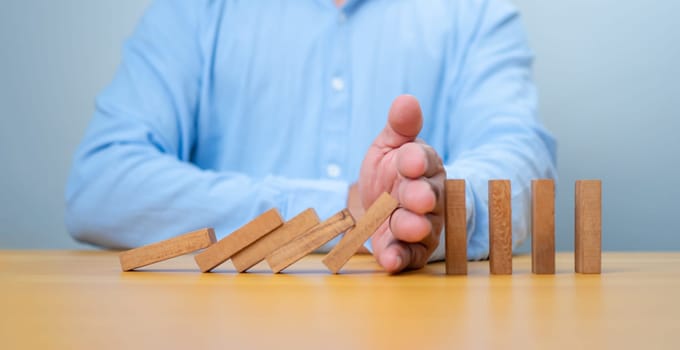 Businessman hand Stopping Falling wooden Blocks or Dominoes, Business, Risk Management, Solution, Insurance and strategy Concepts, Risk and strategy in business.