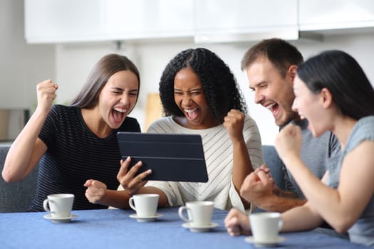 Four excited interracial friends watching media on tablet in the kitchen at home