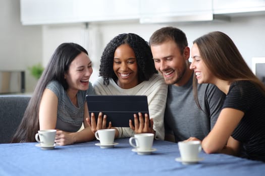 Four interracial friends watching video on tablet in the kitchen at home