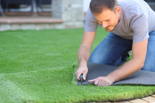 Man installing and cutting artifial turf in the garden at home