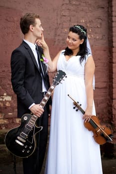 A joyful couple in elegant wedding attire holds guitars, showcasing their love and passion for music