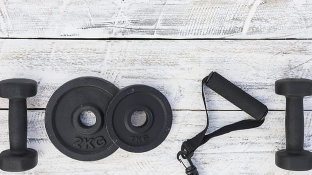 dumbbells weight plates fitness strap white wooden textured background. High resolution photo