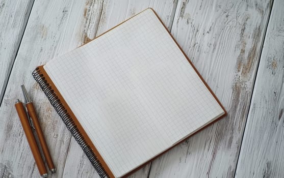 Open blank notebook with grid pages and pens on weathered wooden table, providing ample space for text or design elements.