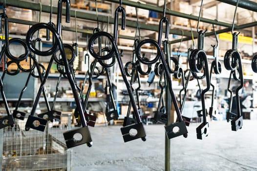 Close-up of black-coated metal parts hanging in a factory or workshop, ready for processing or assembly.
