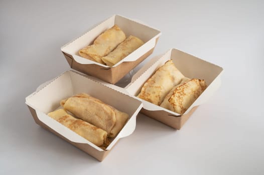 Three takeout boxes filled with neatly folded crepes, ready for delivery or takeaway, photographed against a plain background.