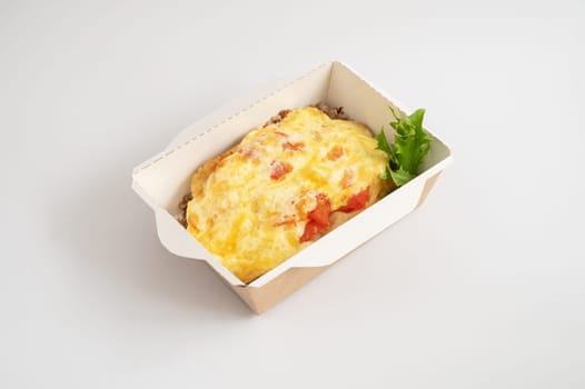 Takeout meal served in biodegradable containers, buckwheat with pork chop with cheese, garnished with greens.