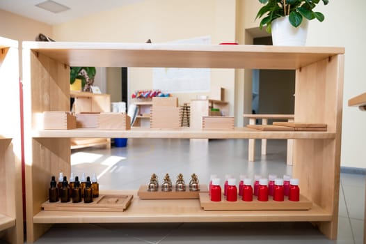 Organized Montessori classroom shelf featuring educational materials like wooden blocks, bells, dropper bottles, and red liquid containers for hands-on learning.