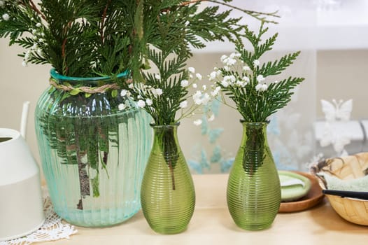 A table setting with green glass vases filled with ferns and white flowers, creating a fresh and natural home decor.