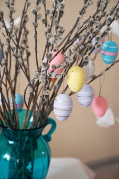 Decorative Easter eggs in various pastel colors hang on pussy willow branches arranged in a vase, creating a festive Easter centerpiece.