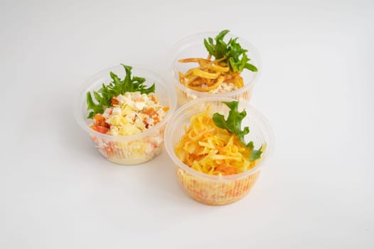 Three clear plastic containers with different salads and fries, garnished with fresh greens.