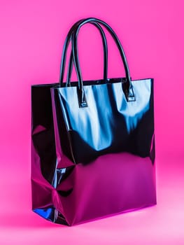 Shiny metallic blue shopping bag with black handles on vibrant pink background, showcasing modern retail style and luxury shopping concept.