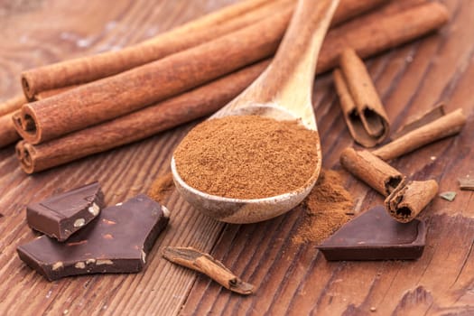 Cinnamon powder on a wooden spoon, cinnamon sticks, and chunks of dark chocolate.